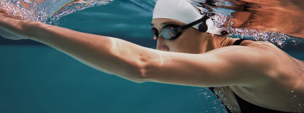 A swimmer in a white cap and goggles mid stroke in a pool.